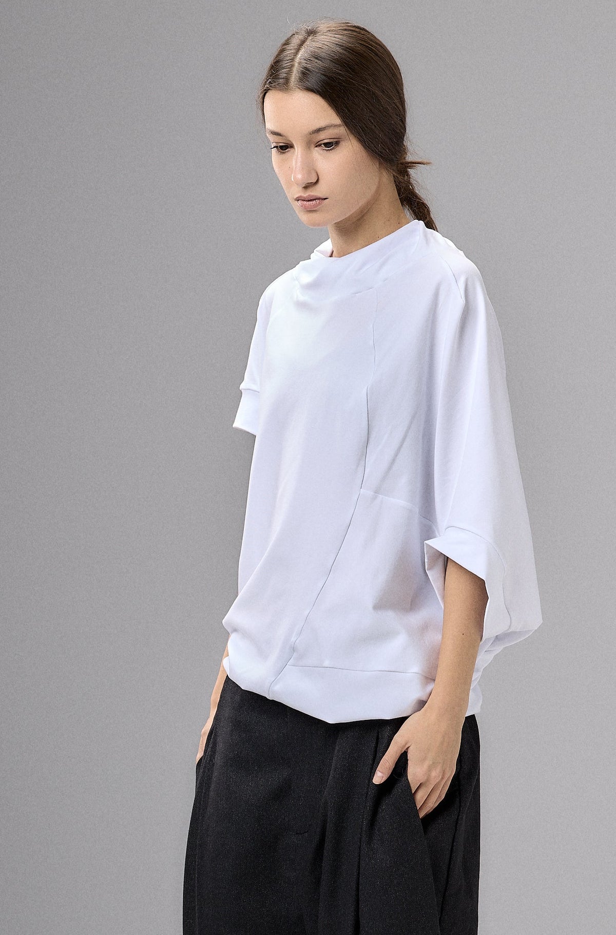 Person wearing a white shirt and black pants against a gray background