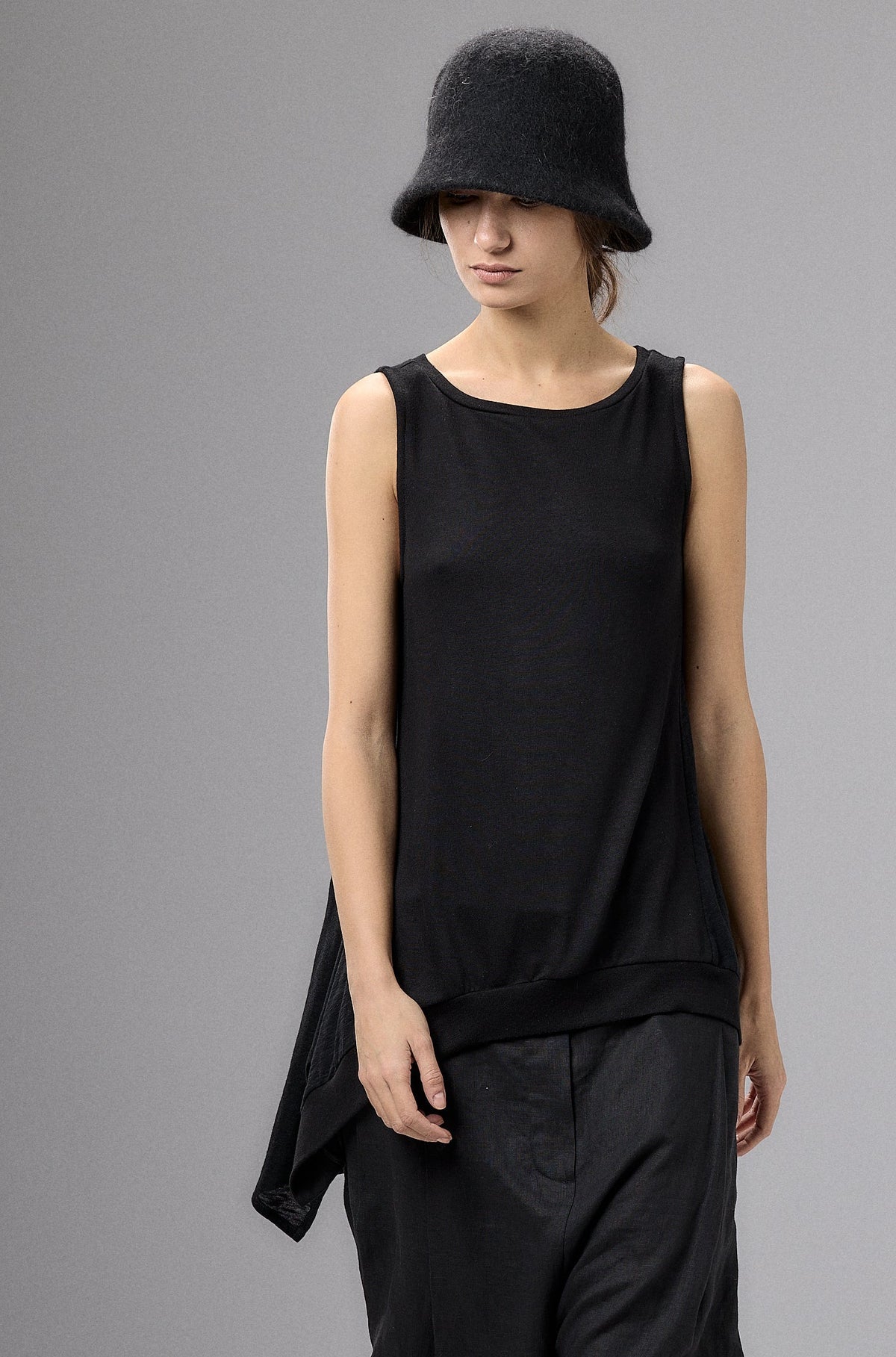 Person wearing a black sleeveless top and pants with a hat against a gray background