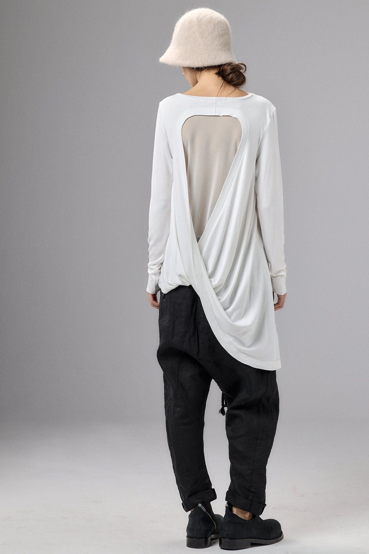 Person wearing a white long-sleeve top with a sheer back panel and black pants on a gray background