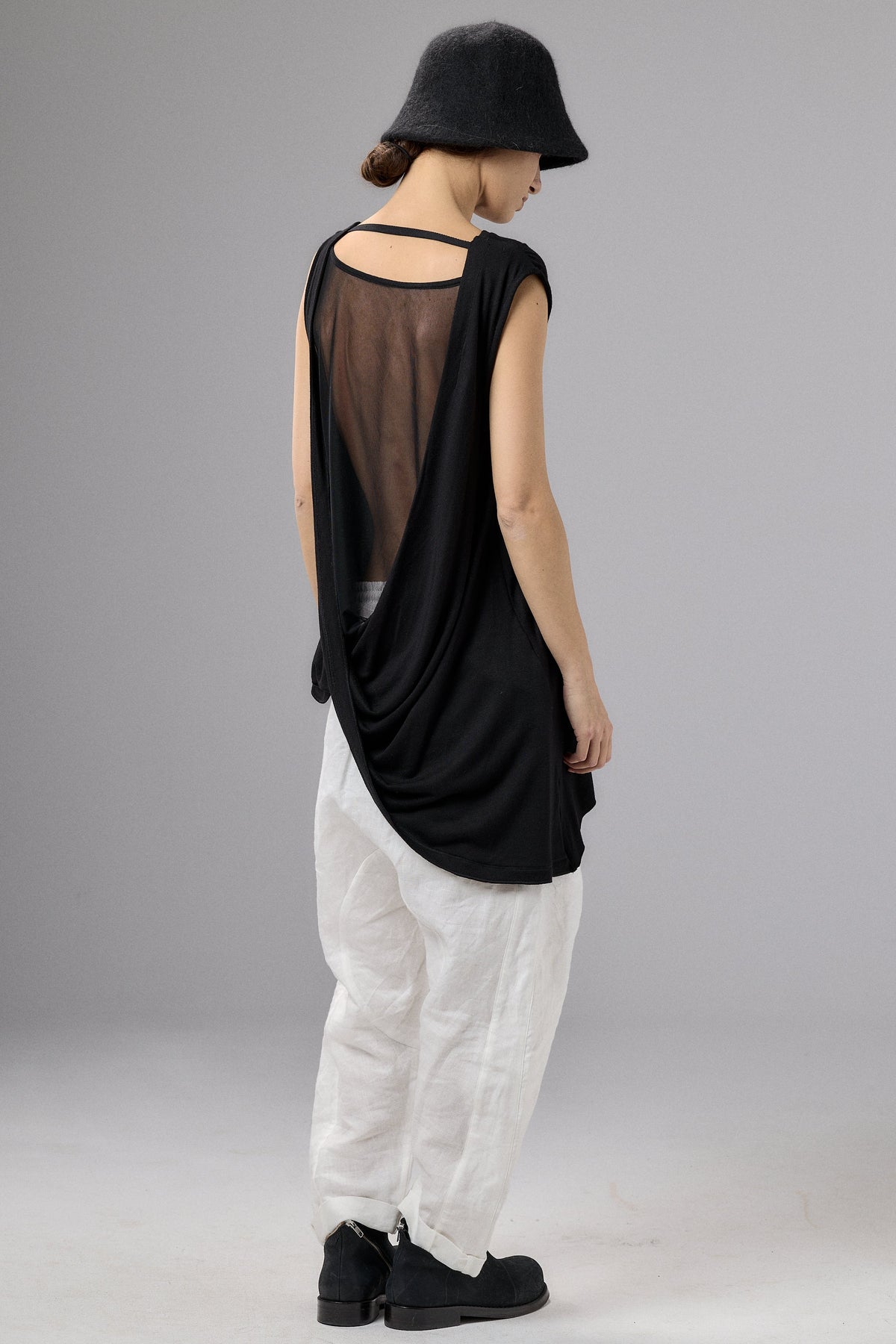 Person wearing a black sleeveless top with sheer panels and white pants on a gray background