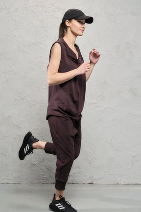 Woman in brown sleeveless top and pants with black cap and shoes against a gray background