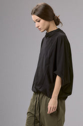 Woman wearing a black shirt and green pants against a gray background