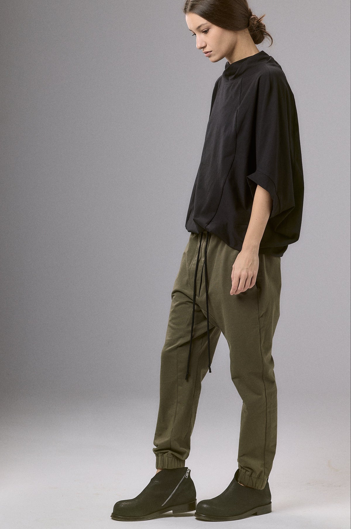 Person wearing a black shirt and green pants standing against a gray background