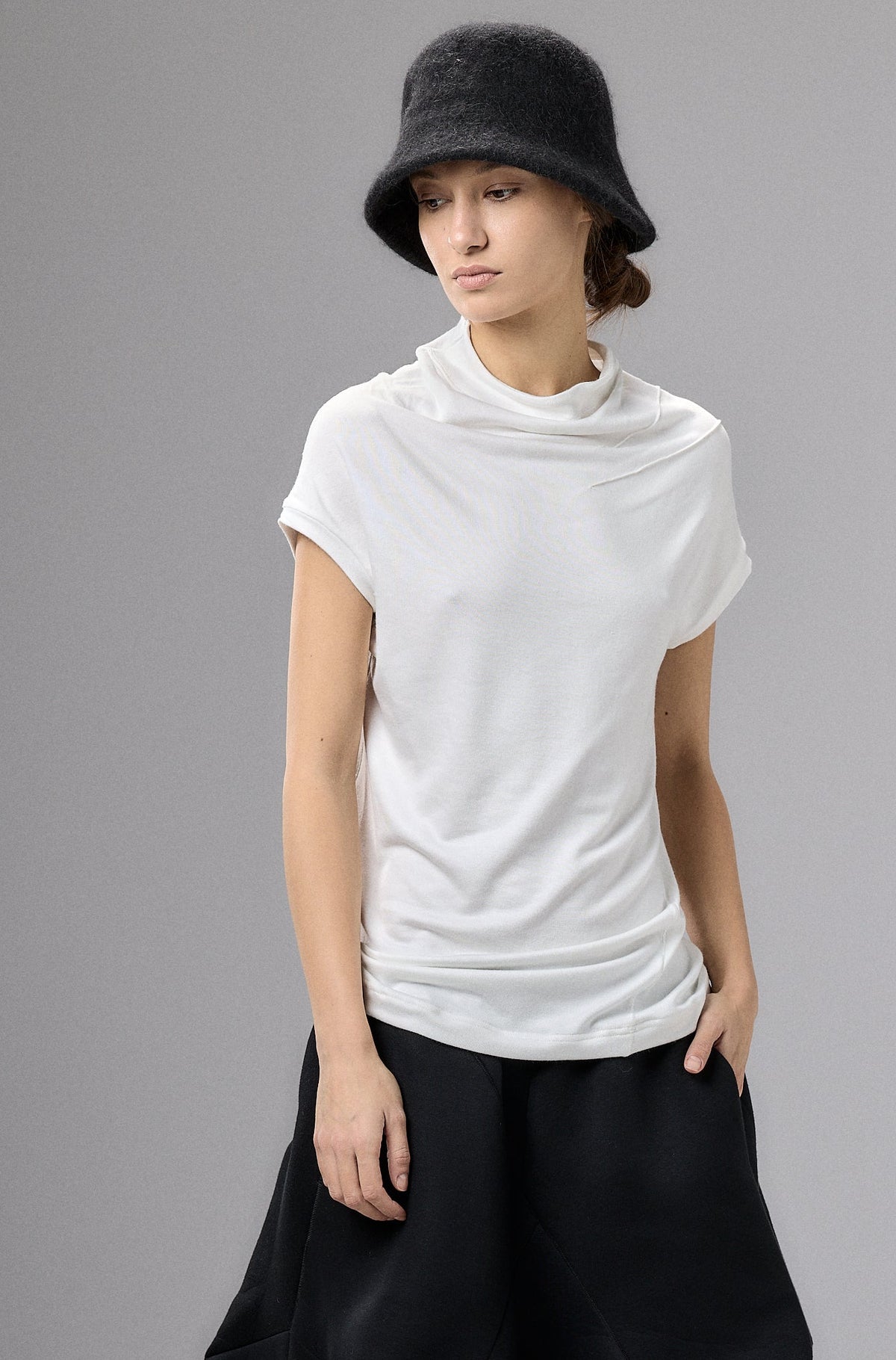 Person wearing a white top and black wide-leg pants with a black hat against a gray background