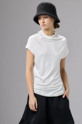 Person wearing a white top and black wide-leg pants with a black hat against a gray background