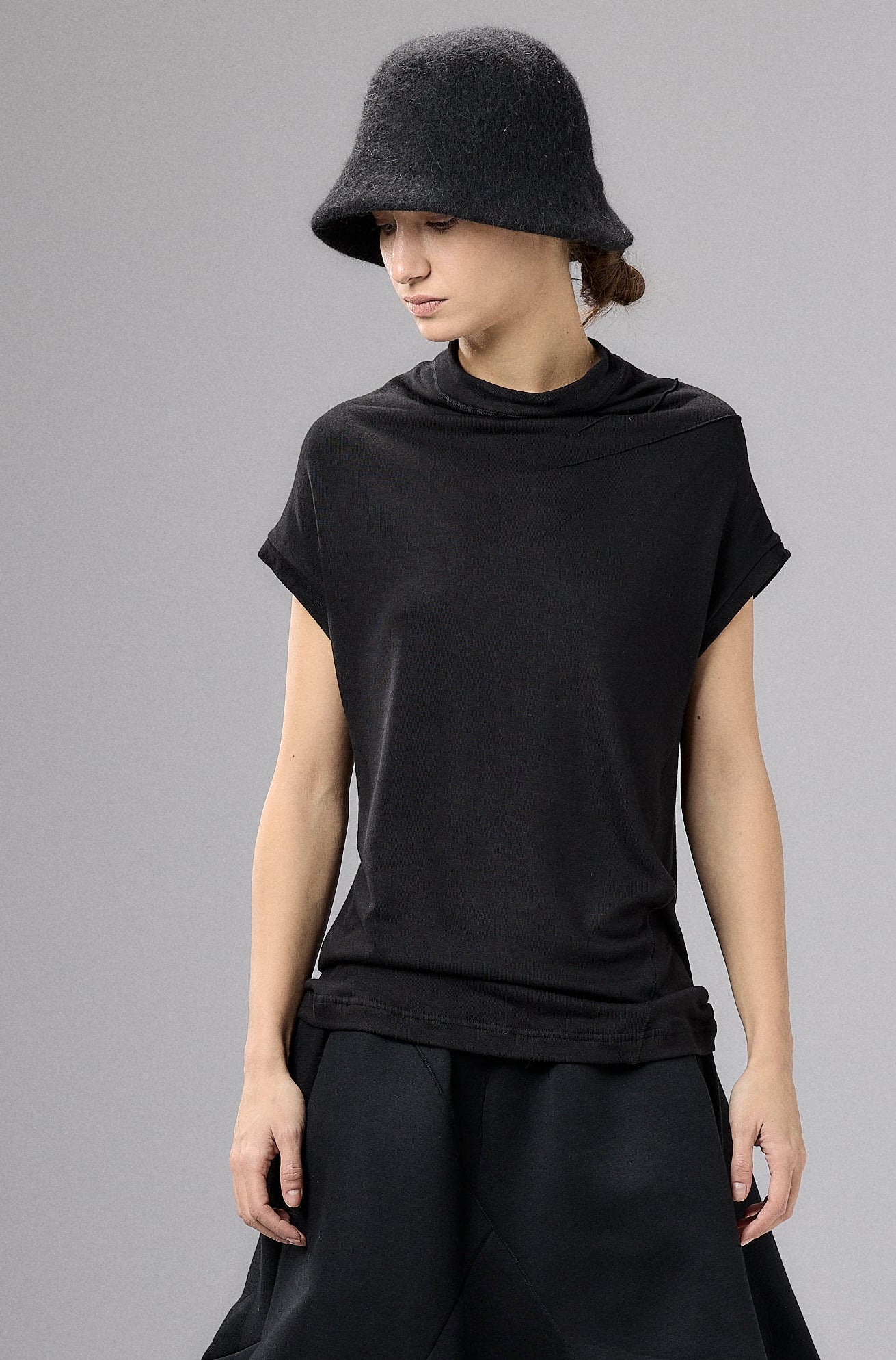 Person wearing a black outfit with a wide-brimmed hat against a gray background