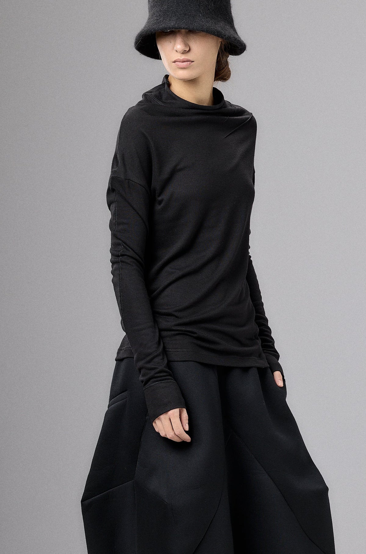 Person wearing a black outfit with wide-leg pants and a hat on a gray background