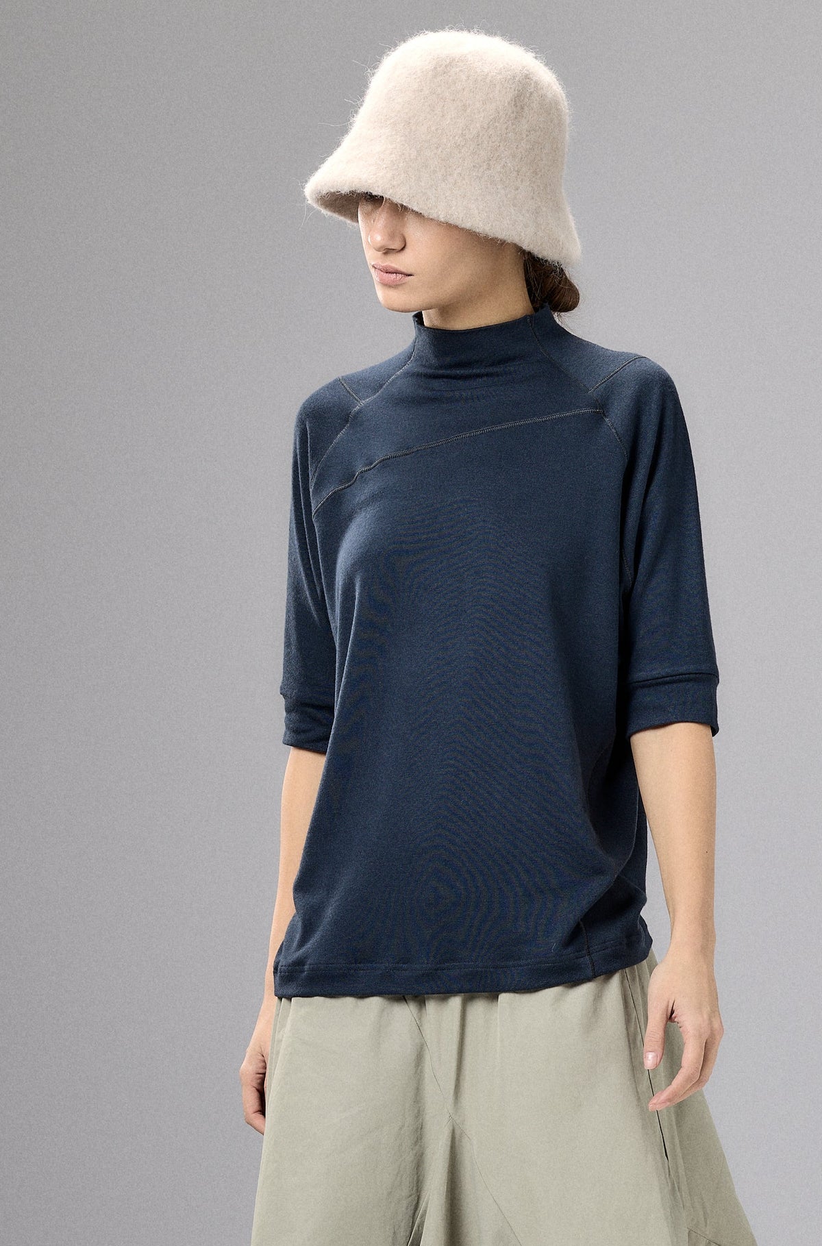 Person wearing a navy top and beige wide-leg pants with a cream hat against a gray background