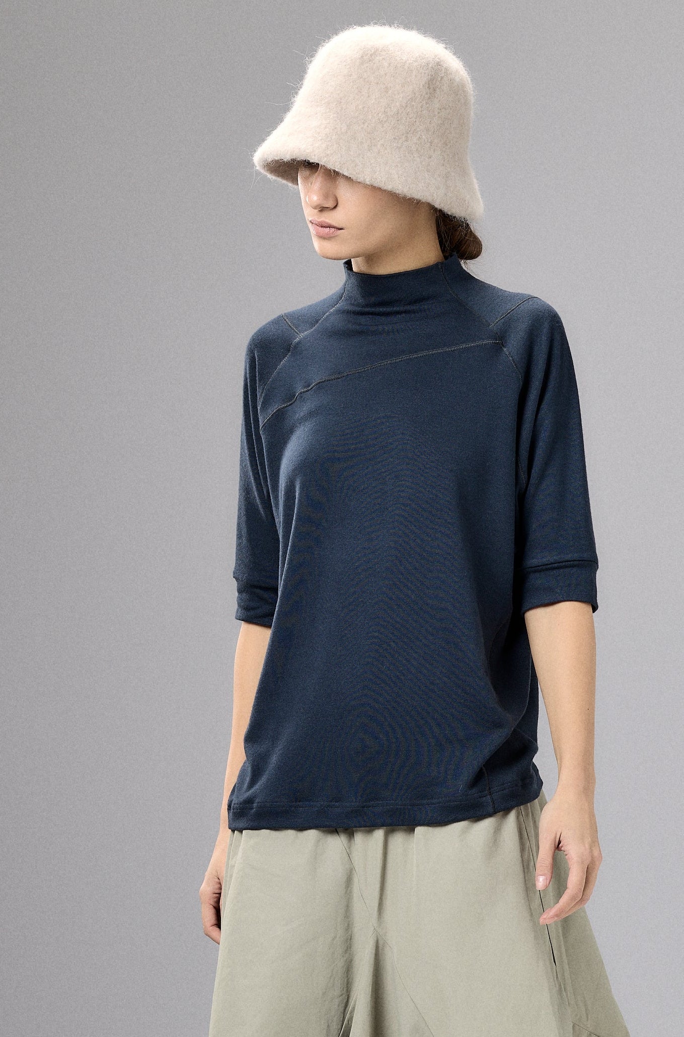 Person wearing a navy top and beige wide-leg pants with a cream hat against a gray background