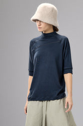 Person wearing a navy top and beige wide-leg pants with a cream hat against a gray background