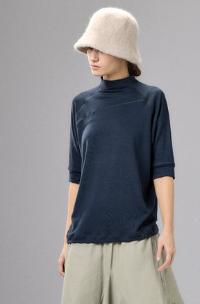 Person wearing a navy top and beige wide-leg pants with a cream hat against a gray background