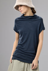 Woman wearing a navy blue cowl-neck top and beige hat on a gray background
