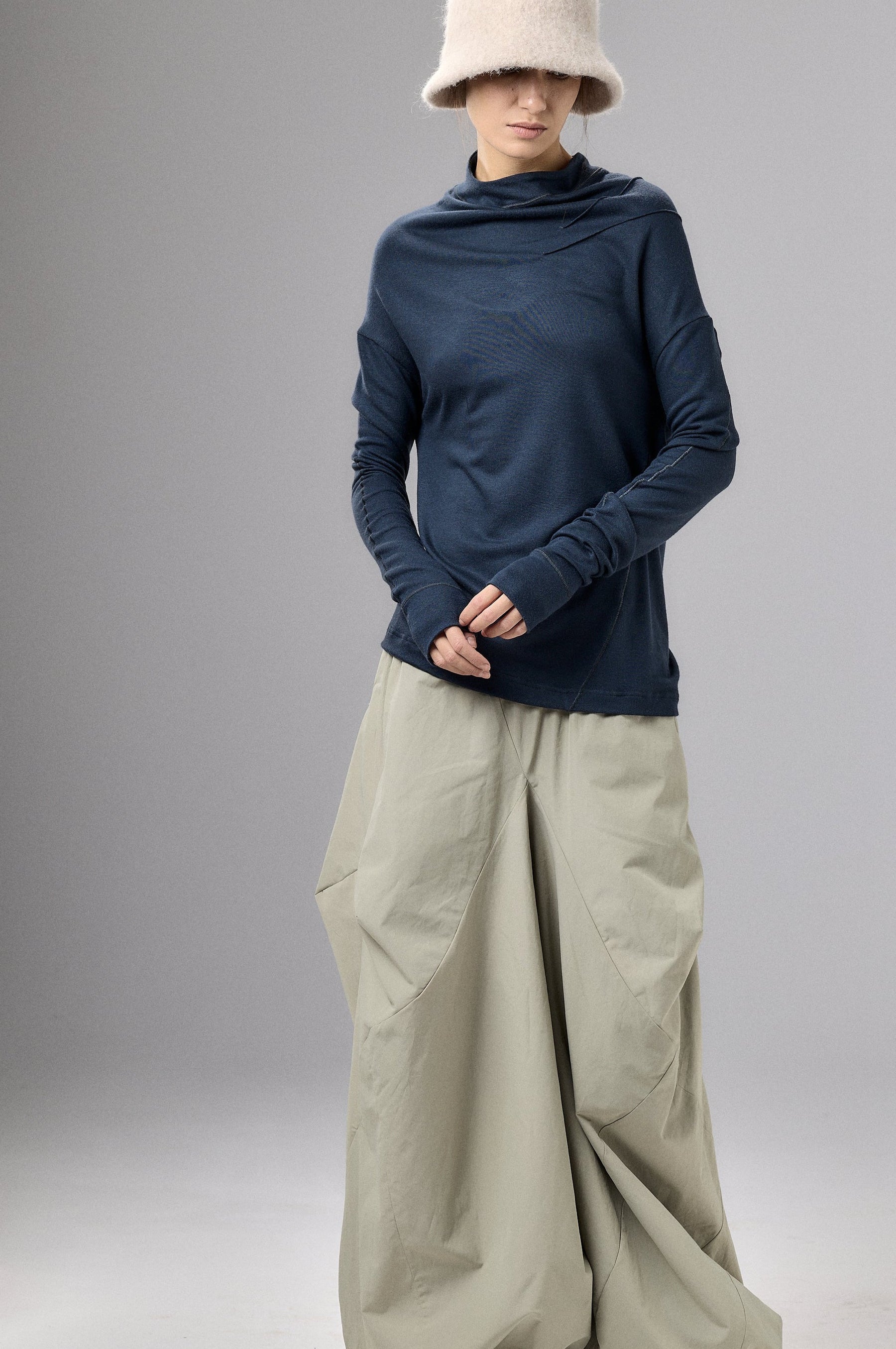 Person wearing a blue top and beige wide-leg pants with a white hat against a gray background