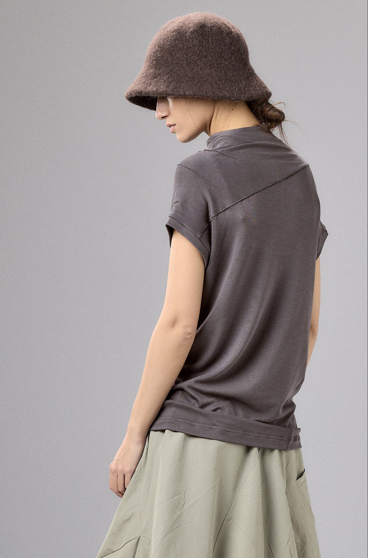 Woman wearing a brown top and light green skirt with a fur hat on a gray background
