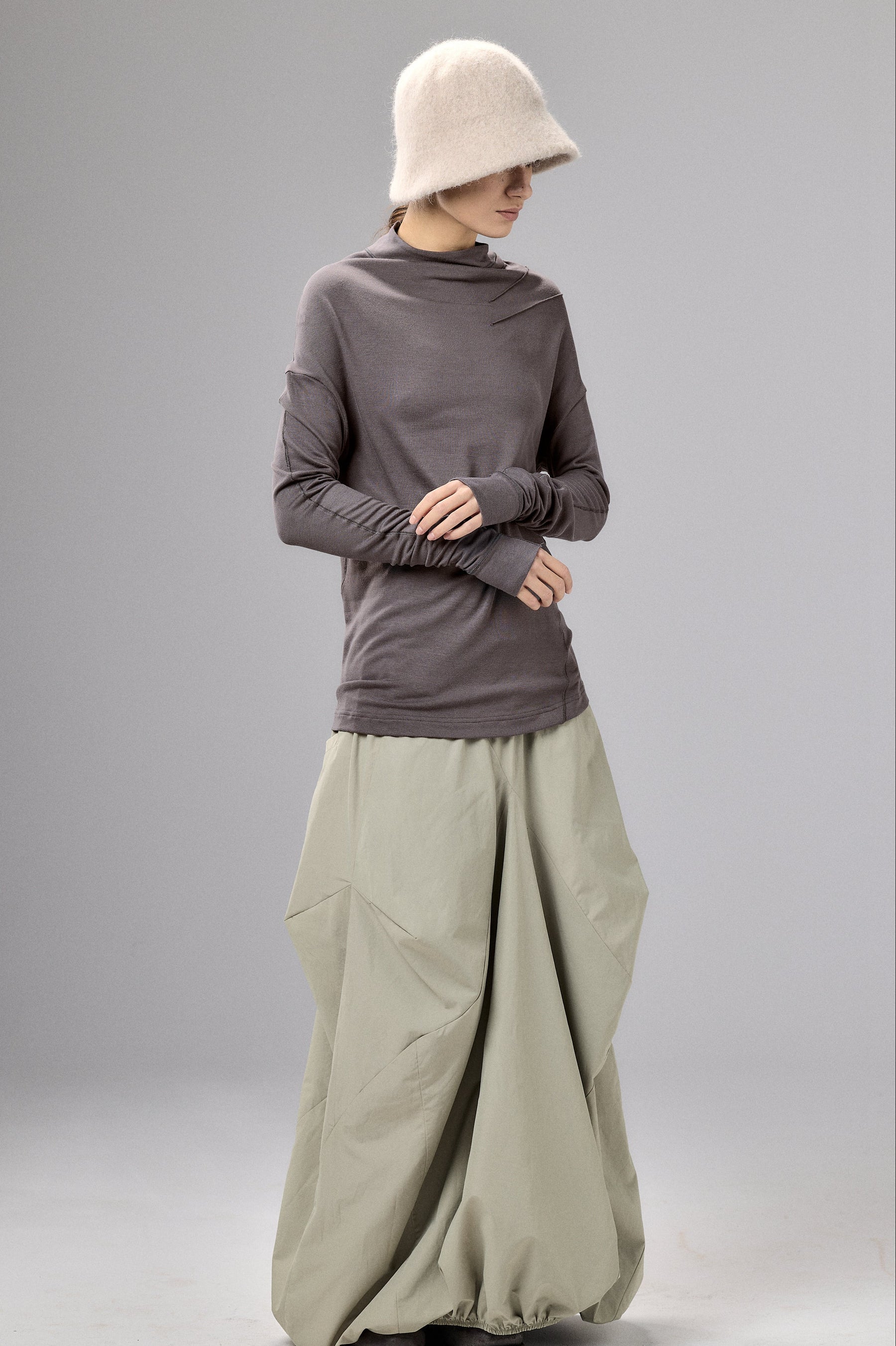 Person wearing a long-sleeve gray top and light green wide-leg pants on a plain background