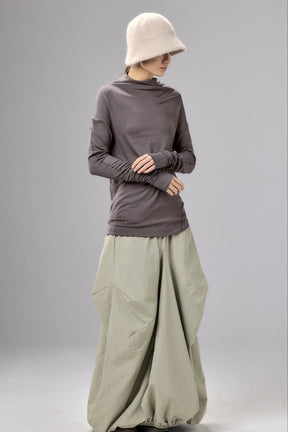 Person wearing a long-sleeve gray top and light green wide-leg pants on a plain background