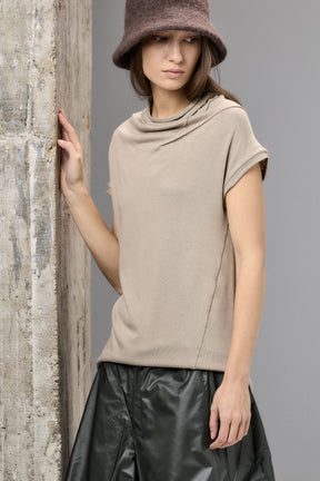 Woman wearing a beige sleeveless top and black leather skirt against a gray background
