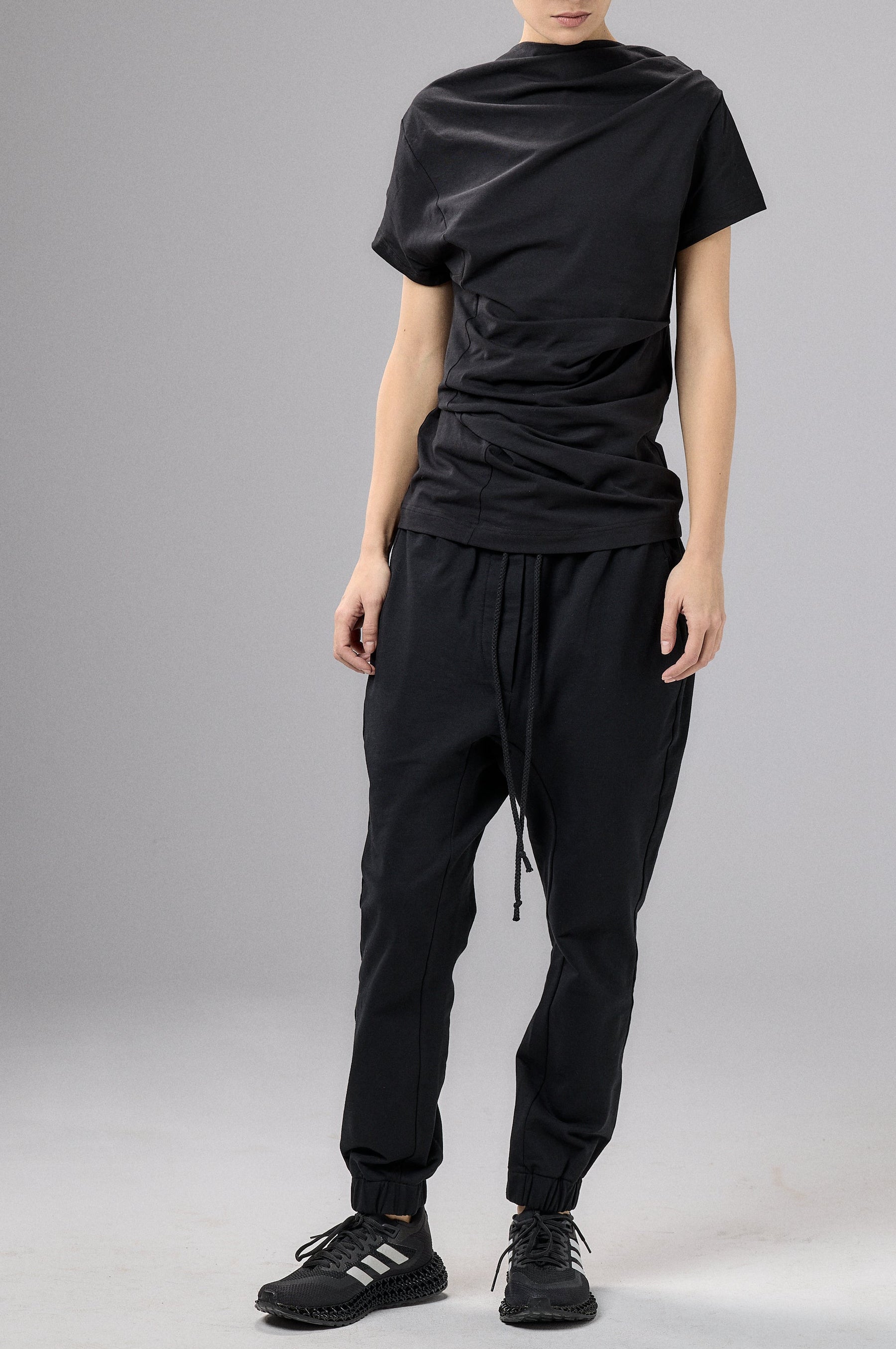 Person wearing a black outfit with a cap on a gray background