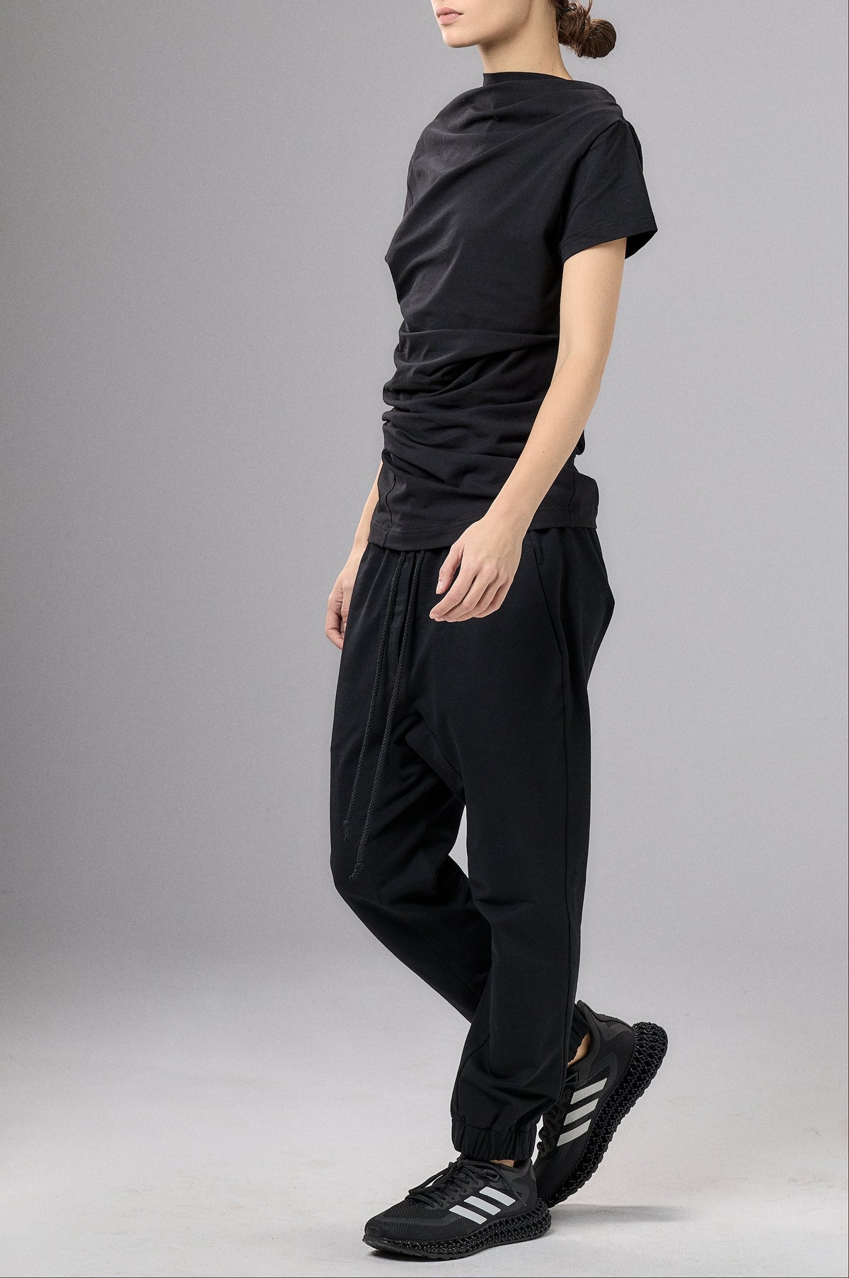 Person wearing a black outfit with a cap on a gray background