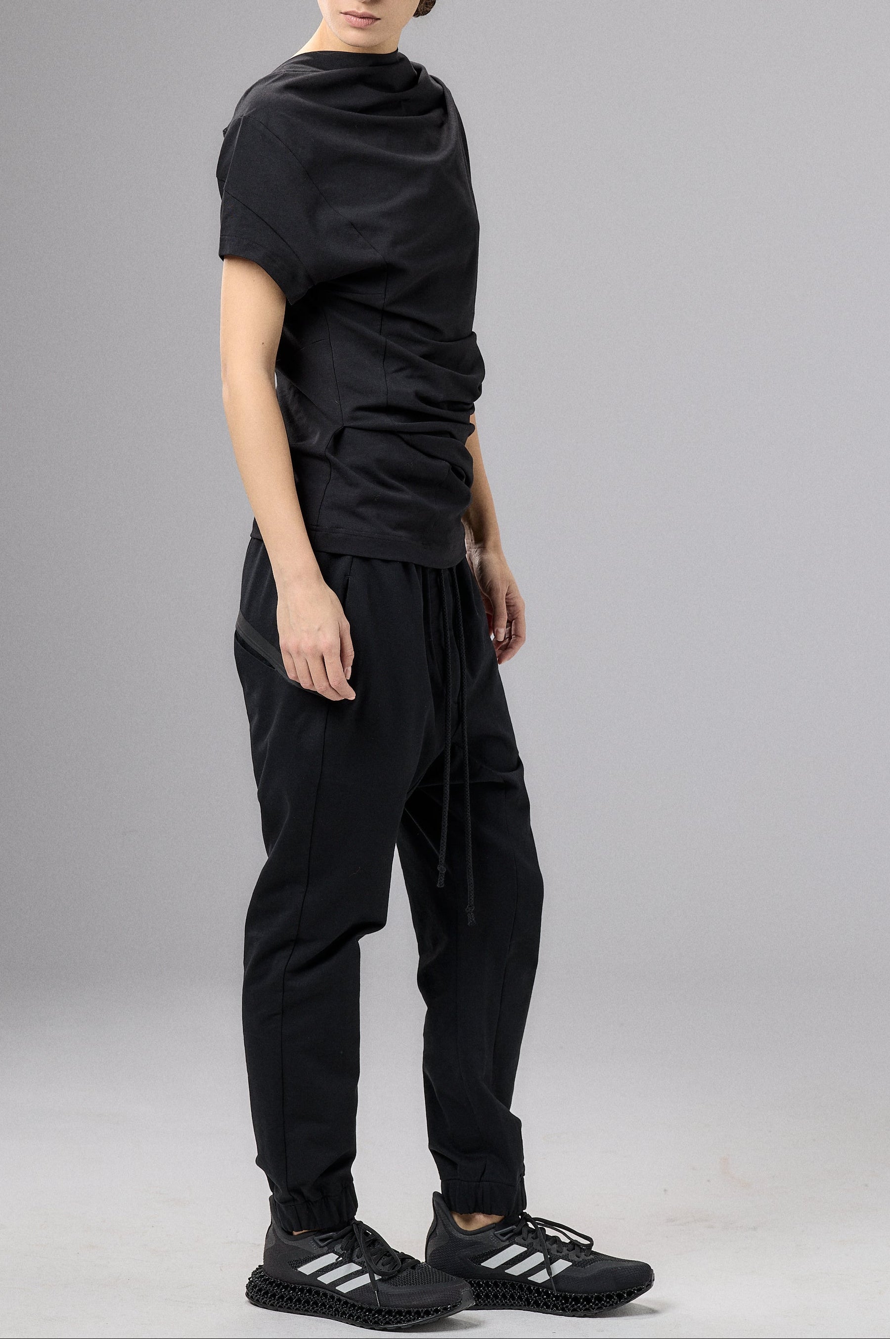 Person wearing a black outfit with a cap on a gray background