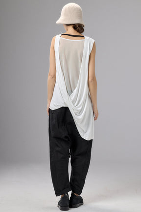 Person wearing a white sleeveless top and black pants with a beige hat on a gray background