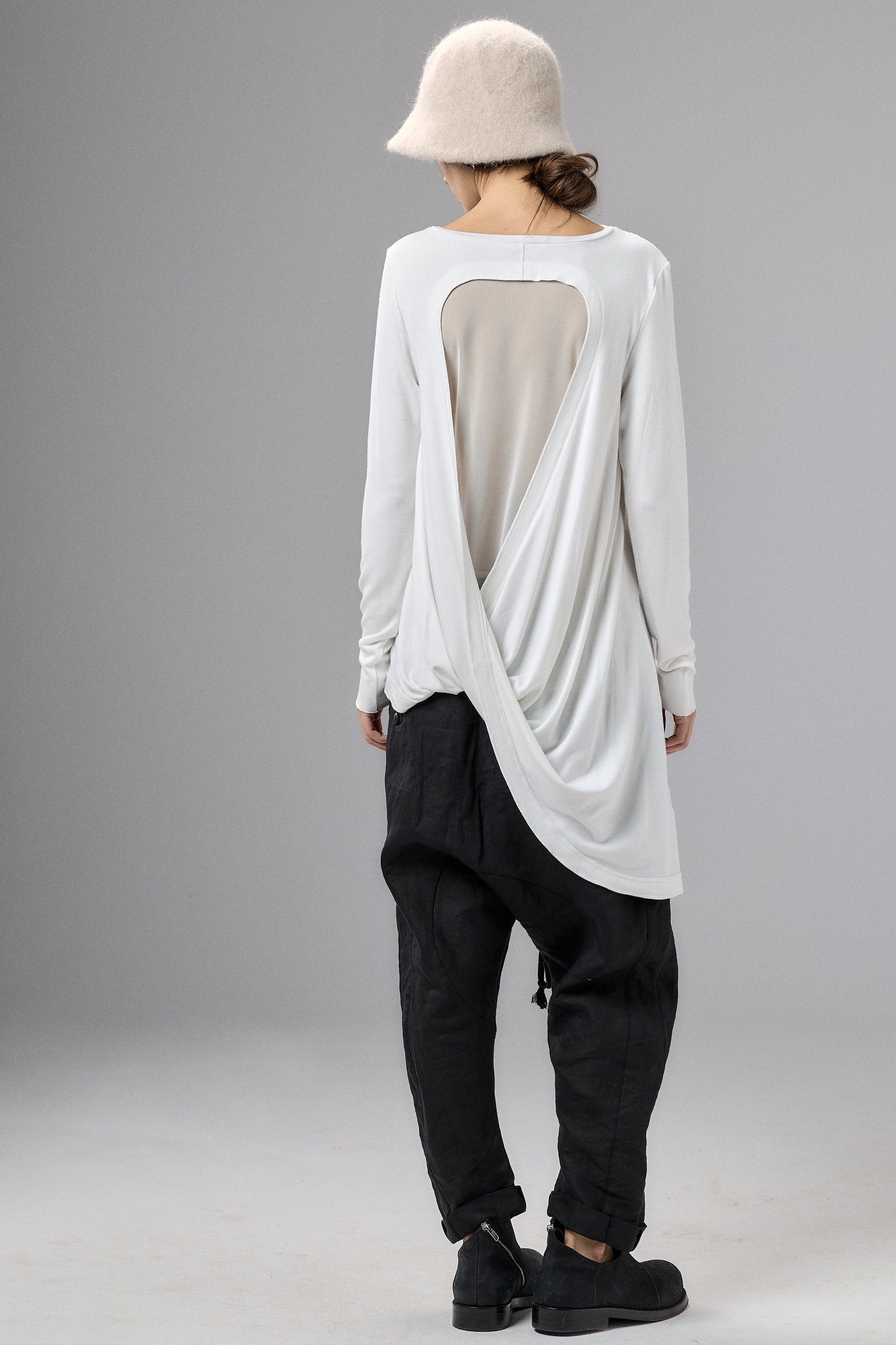 Person wearing a white long-sleeve top with a sheer back panel and black pants on a gray background
