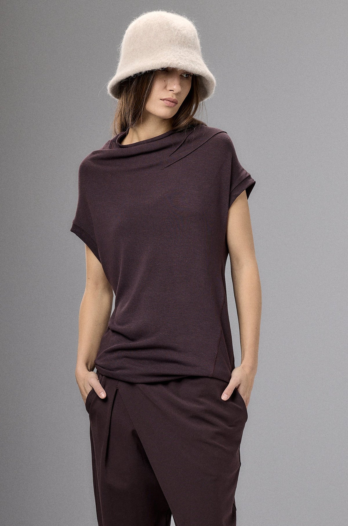Person wearing a brown outfit with a beige hat against a gray background