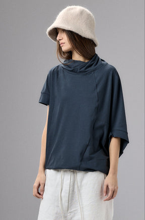 Person wearing a navy t-shirt, white pants, and a beige bucket hat on a gray background