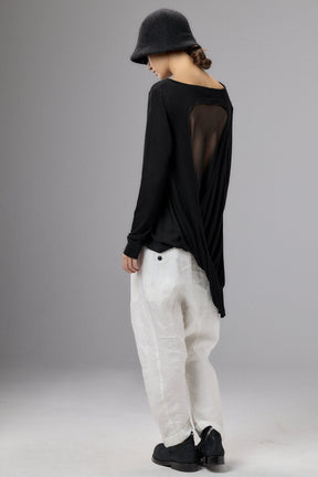 Person wearing a black top with sheer details and white pants on a gray background