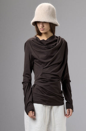 Person wearing a brown long-sleeve top, white pants, and a beige bucket hat against a gray background.
