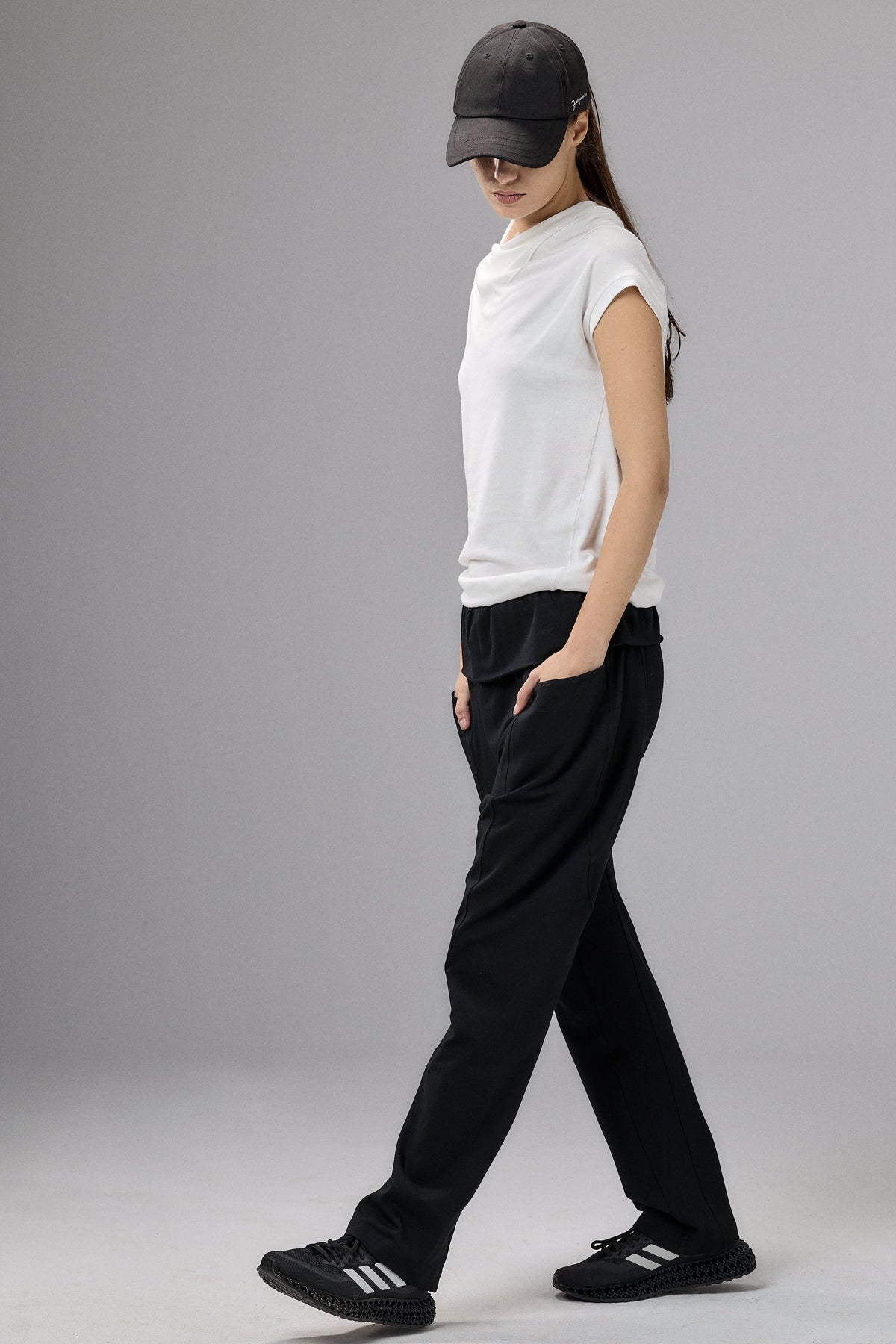 Person wearing a white t-shirt, black pants, and a black cap on a gray background