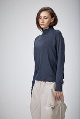 A woman modeling a dark navy blue long-sleeve mock neck top paired with light beige cargo pants, photographed against a neutral light gray studio background.