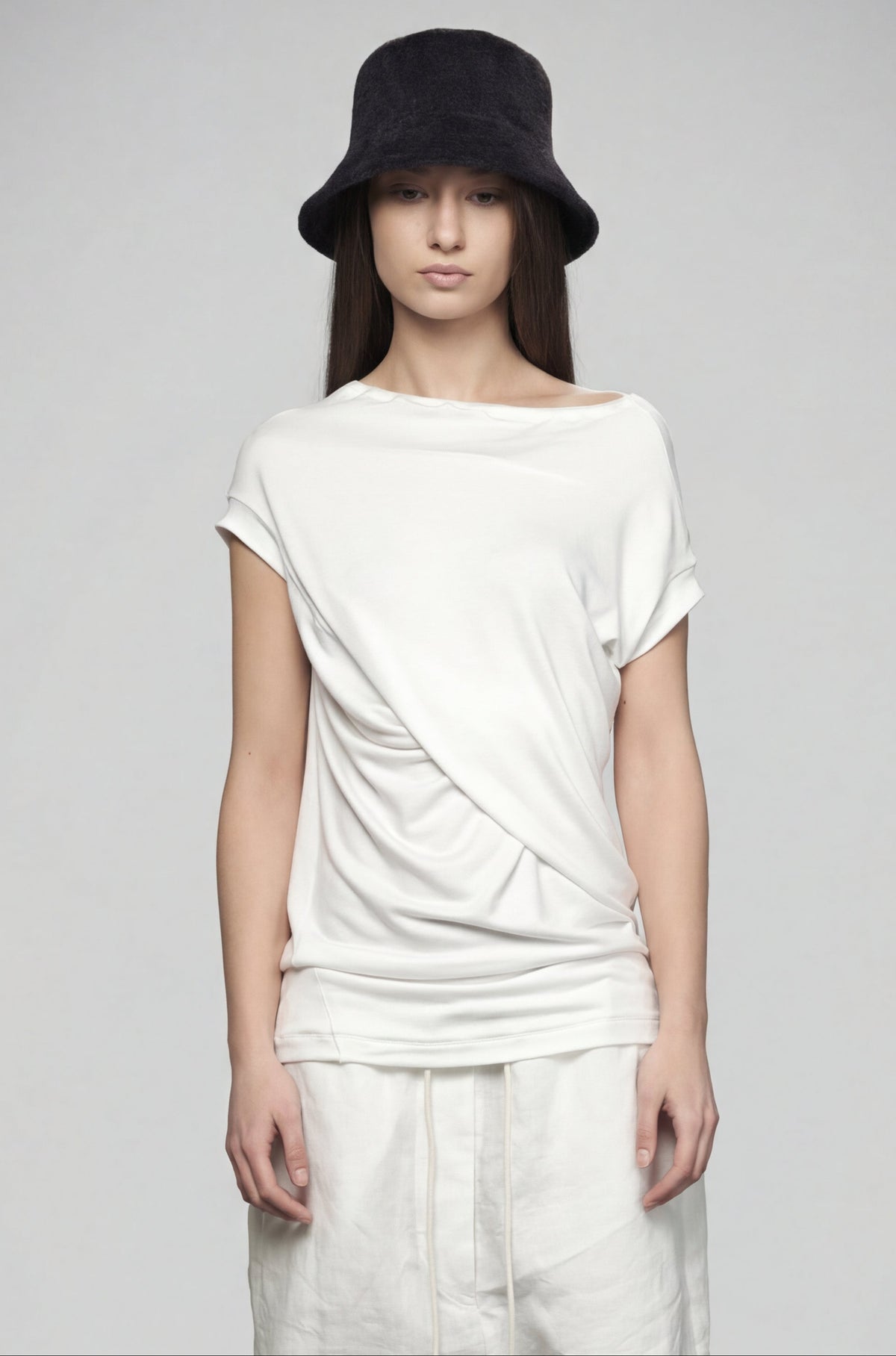 Person wearing a white top and light-colored pants with a black hat on a gray background