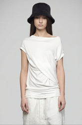 Person wearing a white top and light-colored pants with a black hat on a gray background