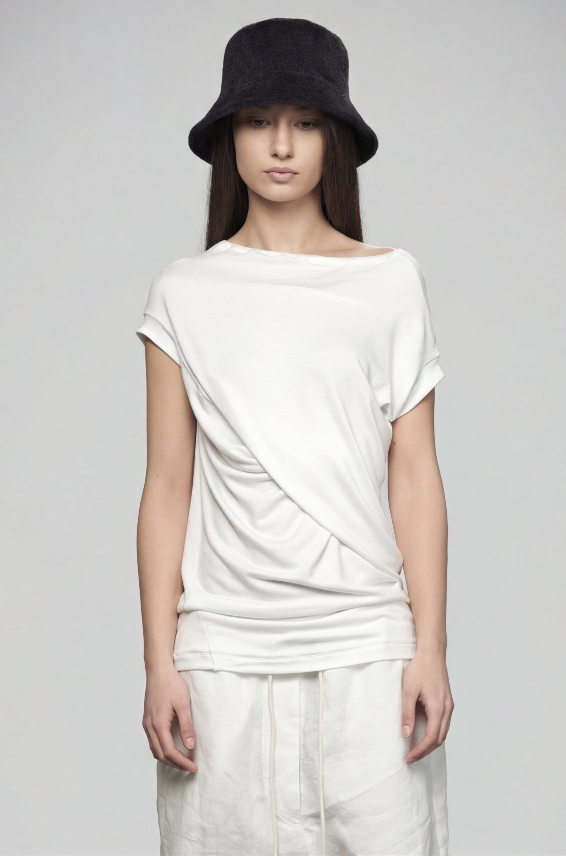 Person wearing a white top and light-colored pants with a black hat on a gray background