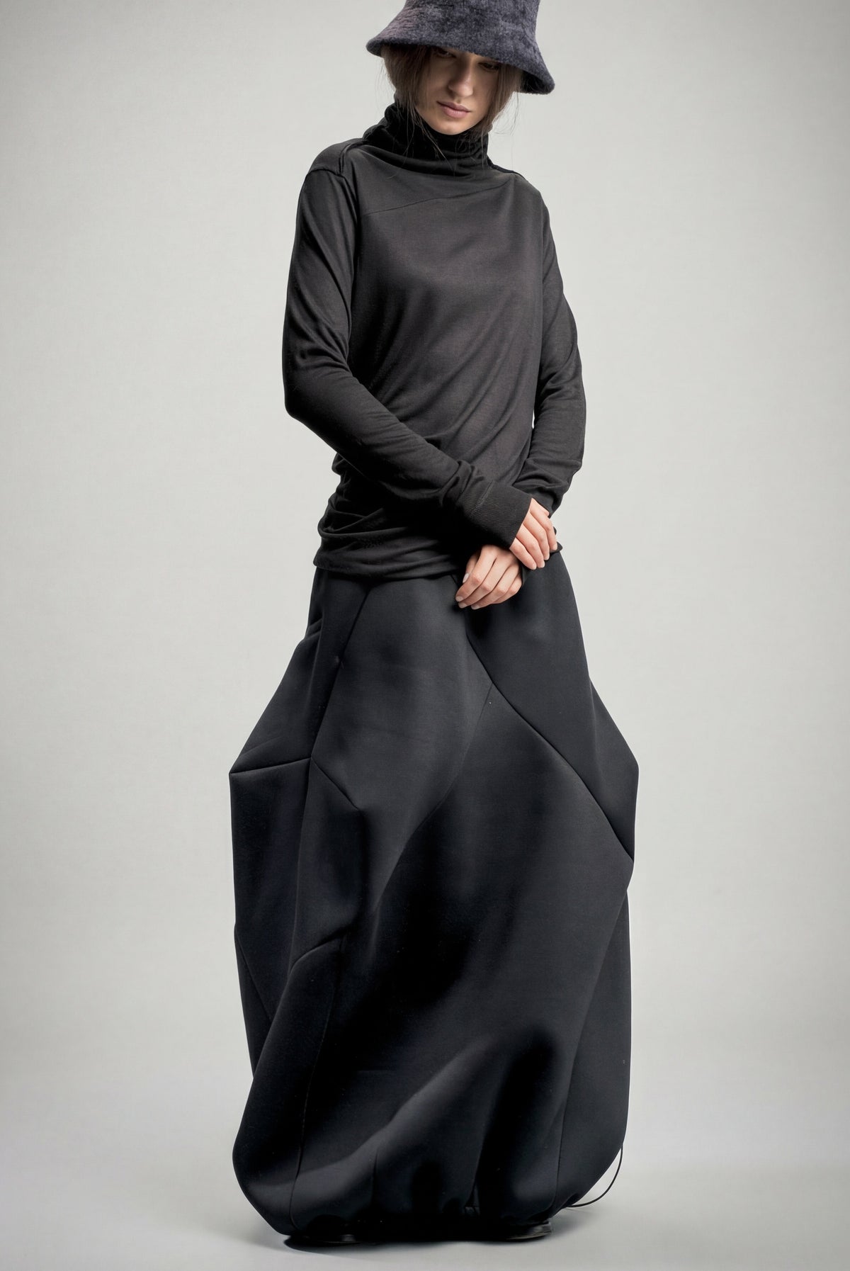 Person wearing a long black neoprene skirt and hat on a gray background