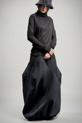 Person wearing a long black neoprene skirt and hat on a gray background