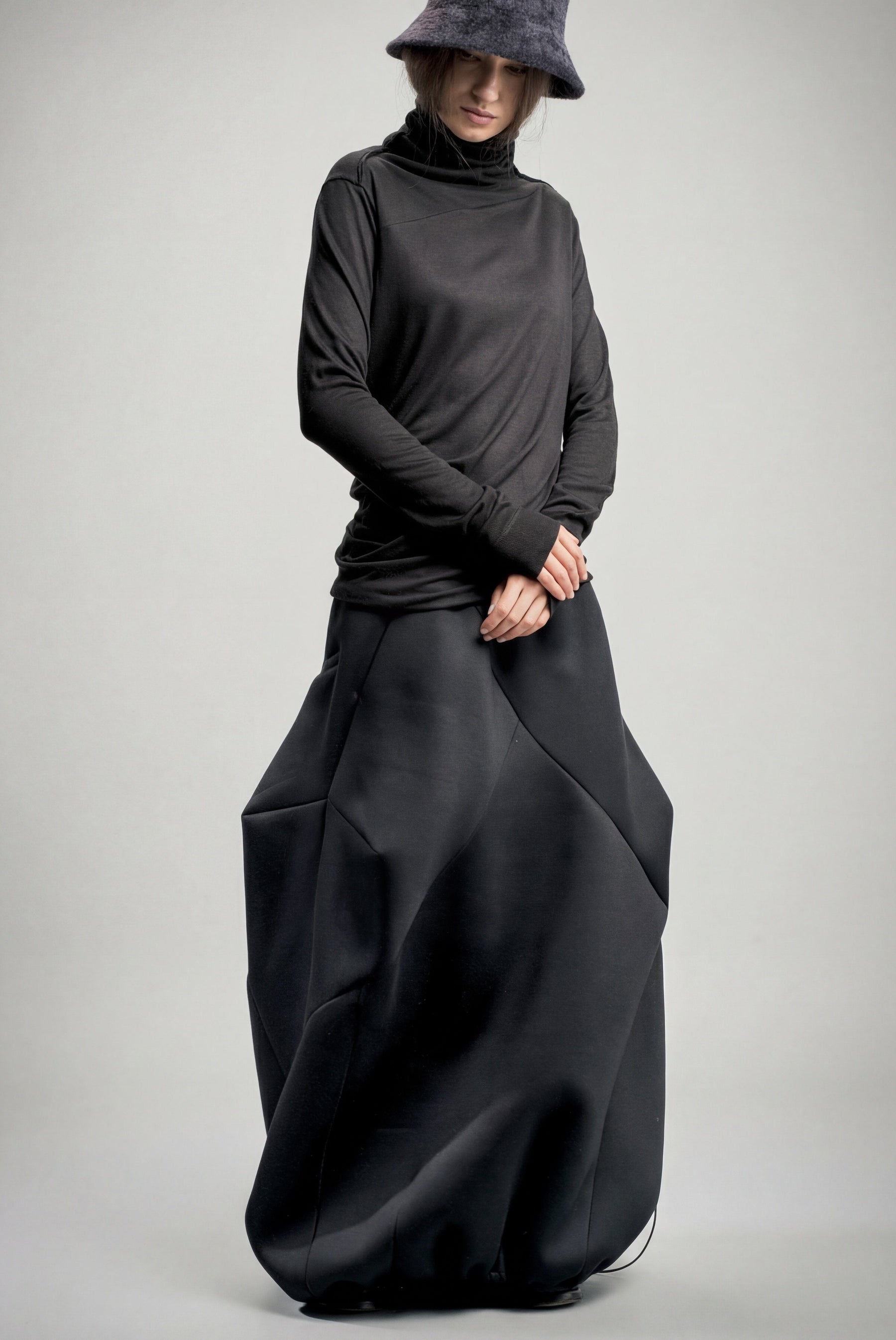 Person wearing a long black neoprene skirt and hat on a gray background