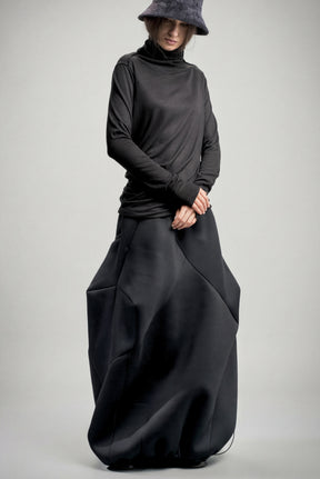 Person wearing a long black neoprene skirt and hat on a gray background